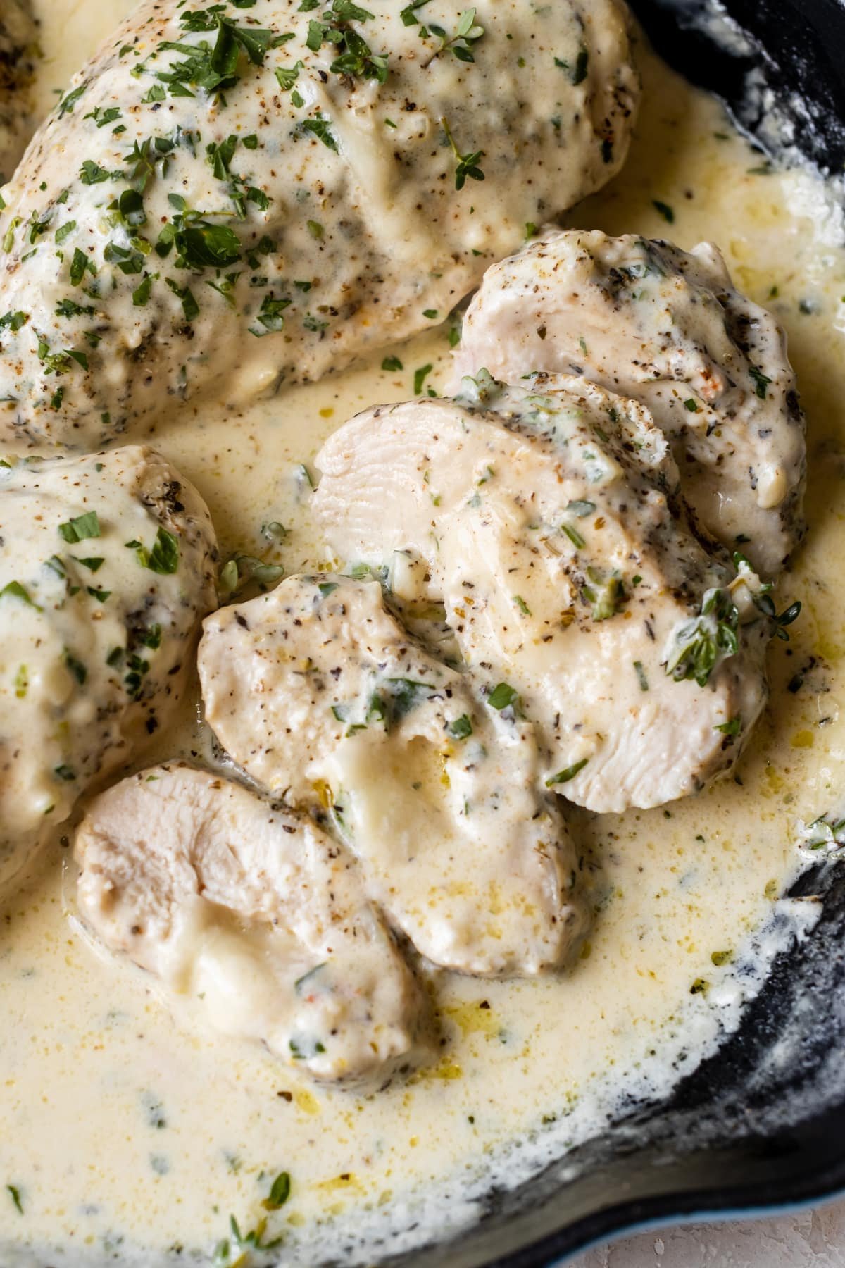 sliced chicken stuffed with cheese covered in cream sauce in a cast iron pan.