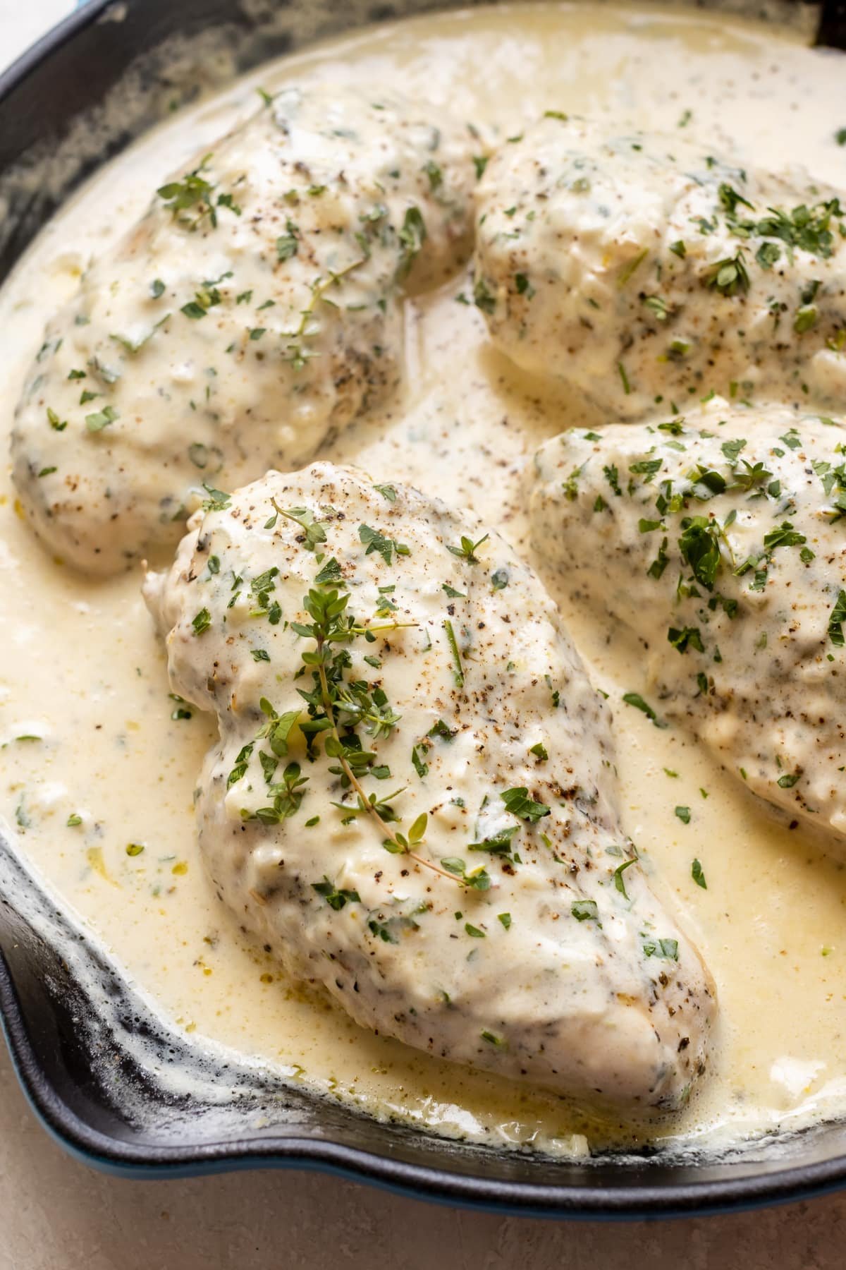 chicken in a pan with a cream sauce garnished with parsley and thyme. 
