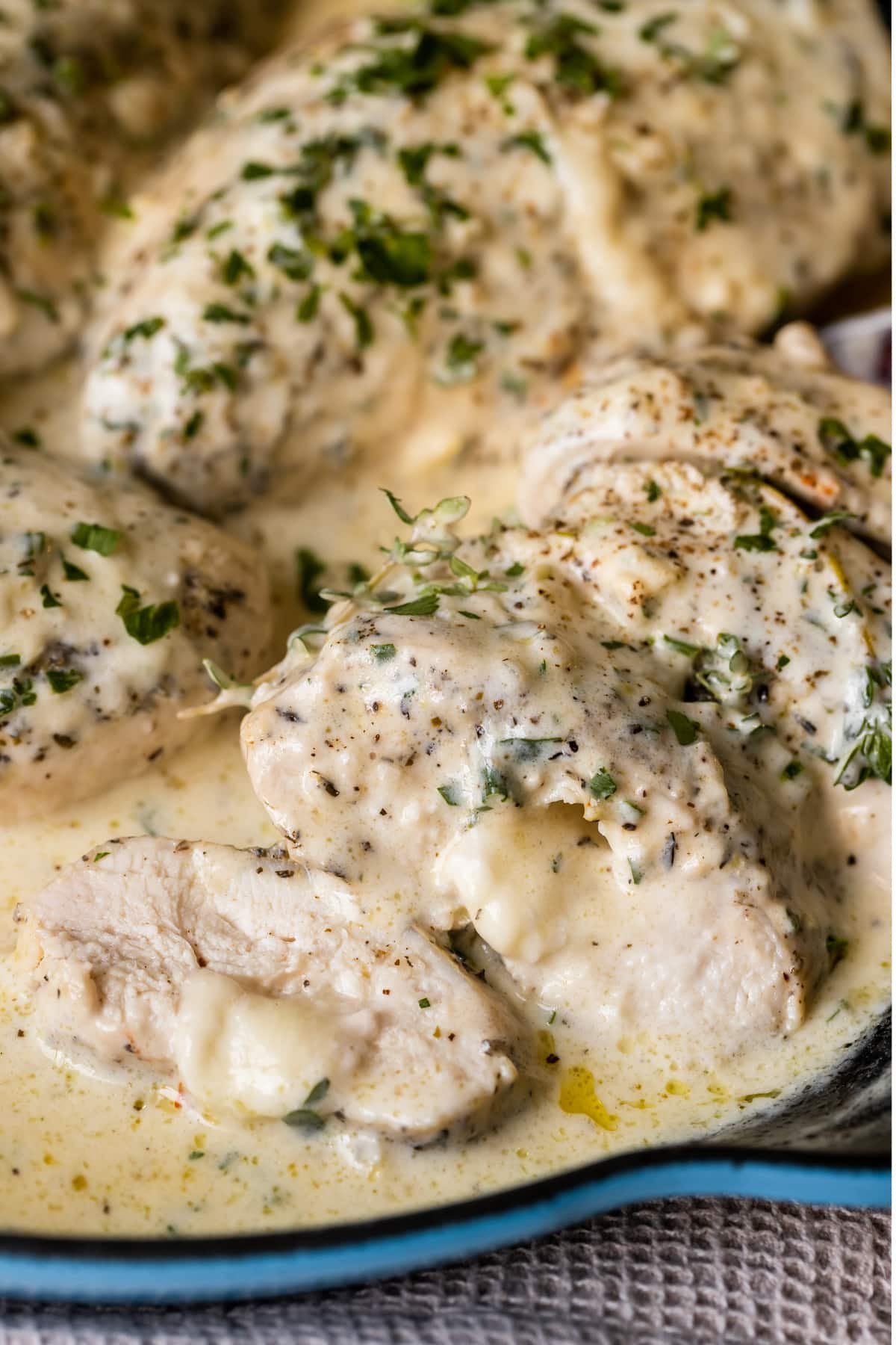 sliced chicken stuffed with cheese covered in cream sauce in a cast iron pan.