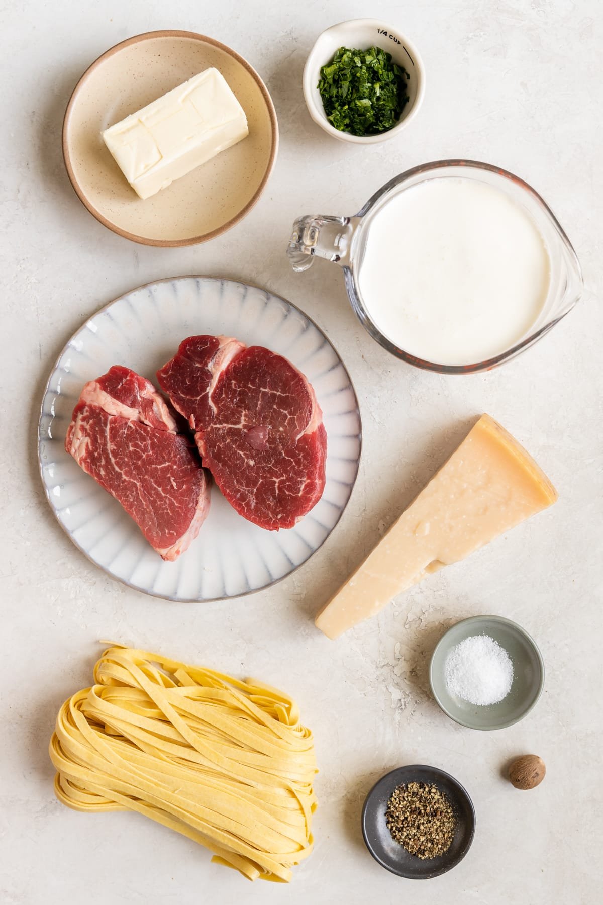 ingredients to make steak Alfredo on plates and in small bowls and measuring cups. 