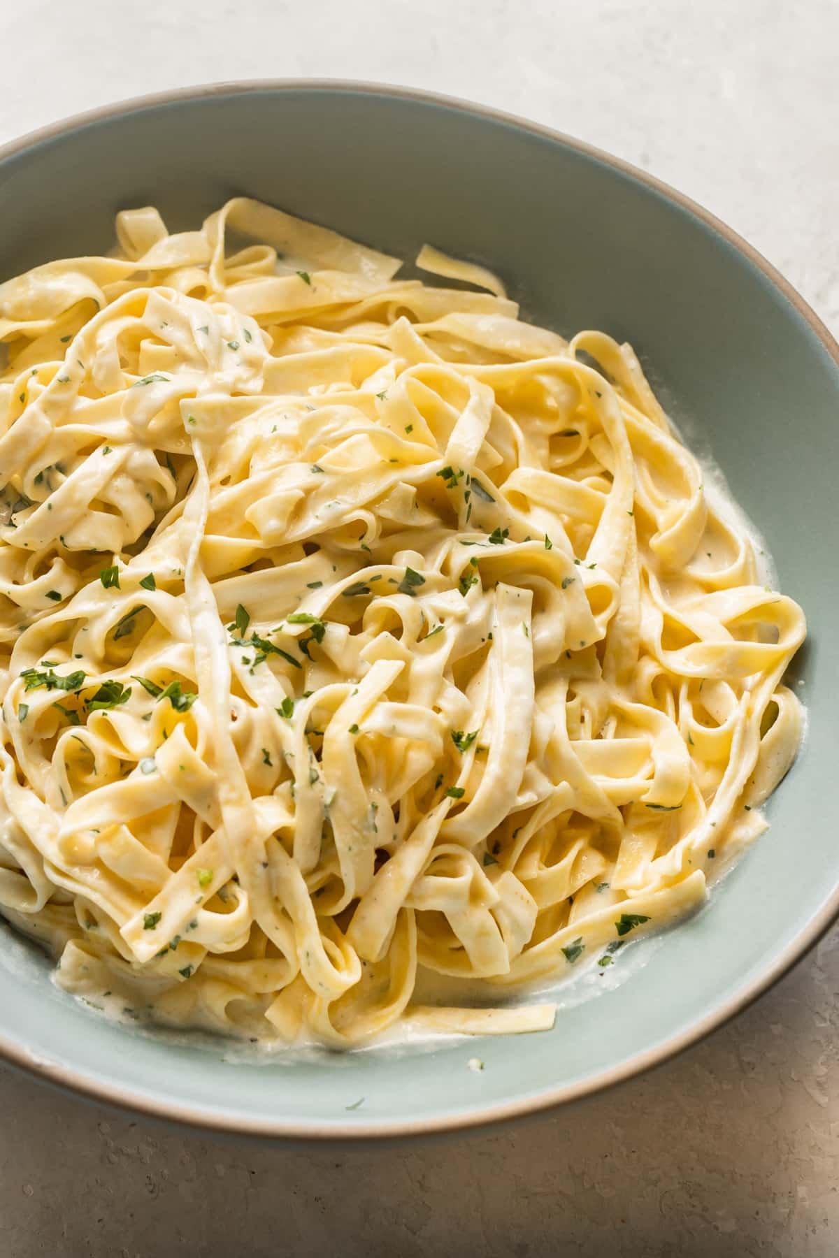 fettuccine pasta tossed with Alfredo sauce in a blue bowl.