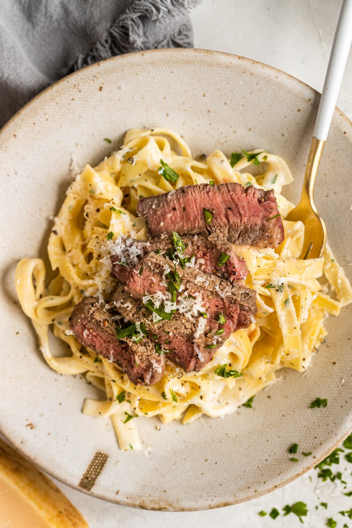 pasta in a bowl topped with steak and garnished with Parmesan cheese and fresh parsley. 