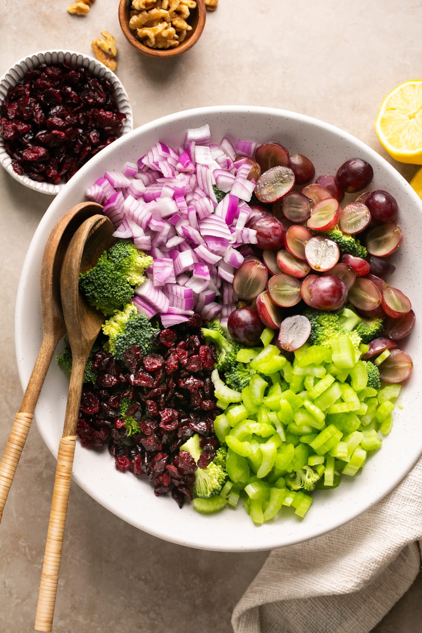 broccoli, cranberries, grapes and celery in a large white bowl. 