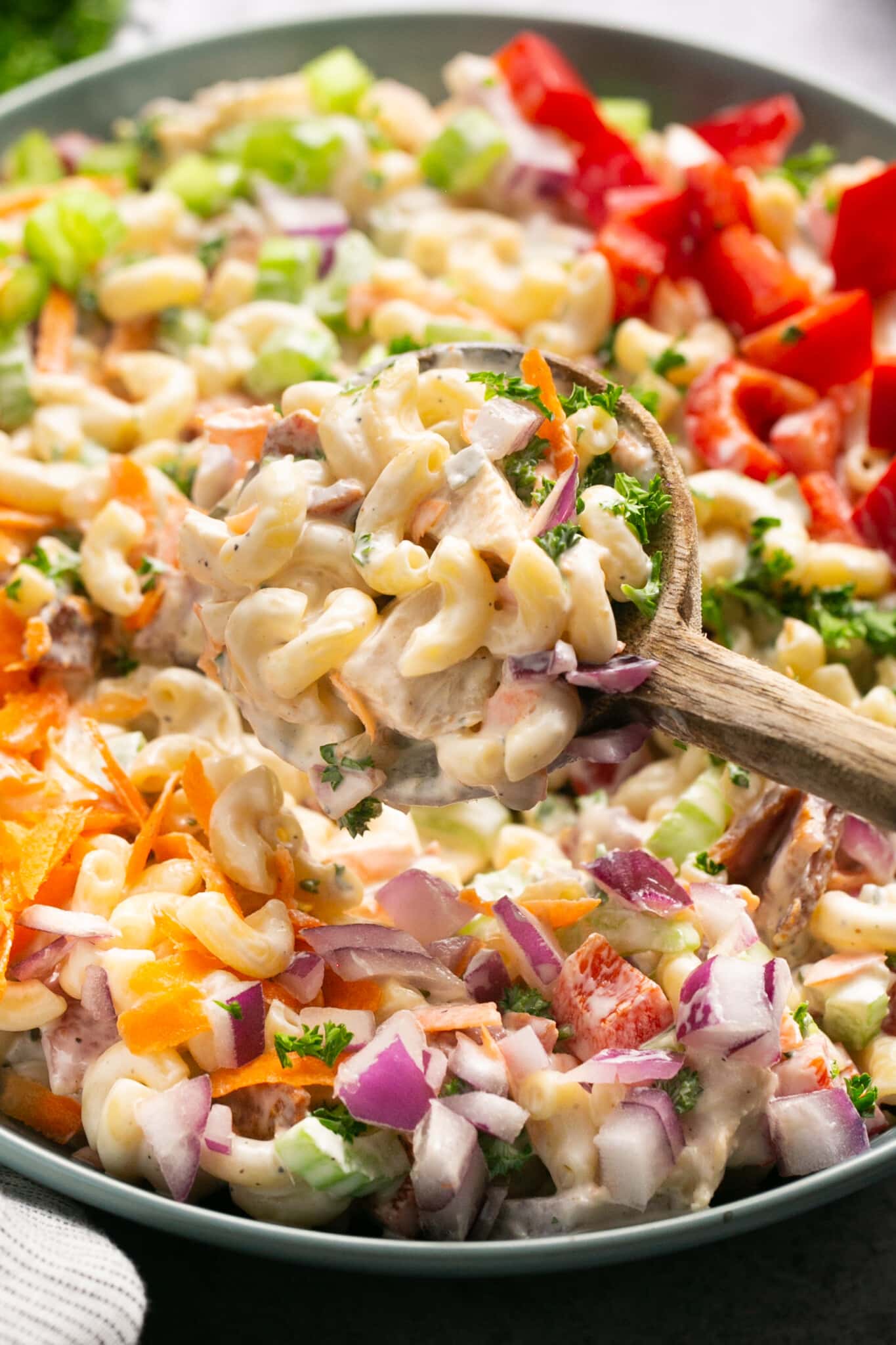 a wooden spoon scooping macaroni salad out of a bowl.