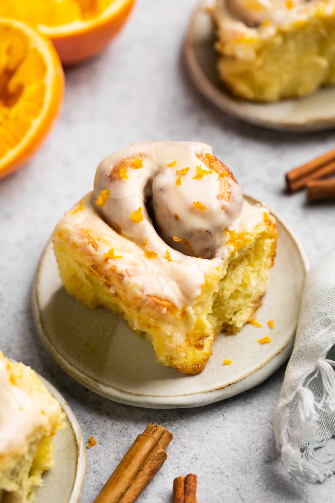 orange cinnamon roll on a plate with a glaze and orange zest on top. 