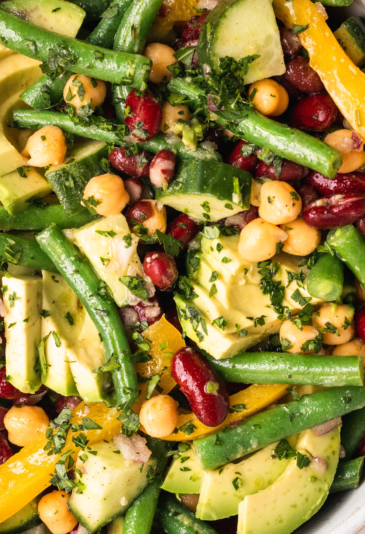 a close up image of a bean salad garnished with sliced avocado and fresh parsley. 