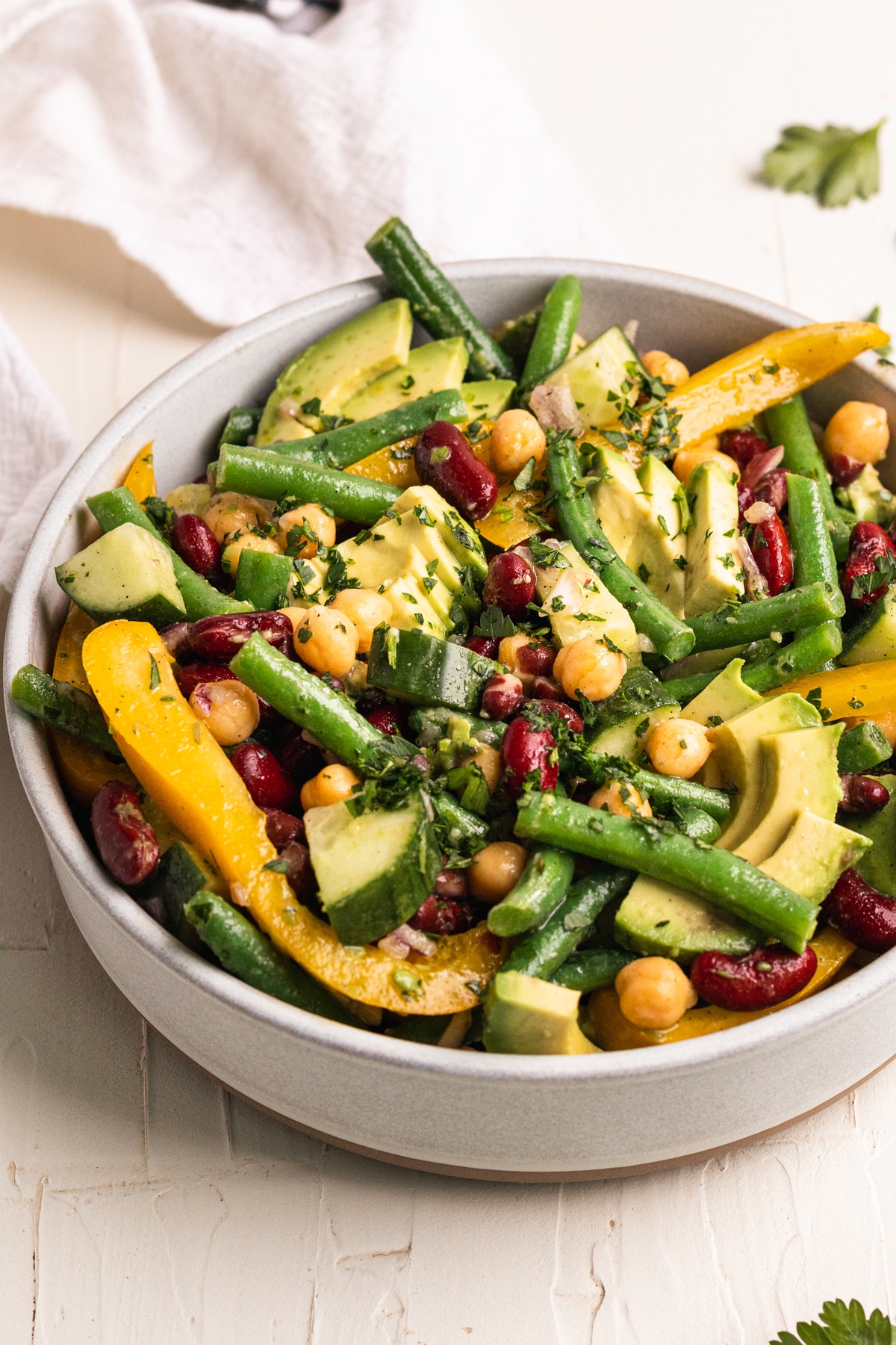 bean salad garnished with sliced avocado and fresh parsley in a white bowl. 