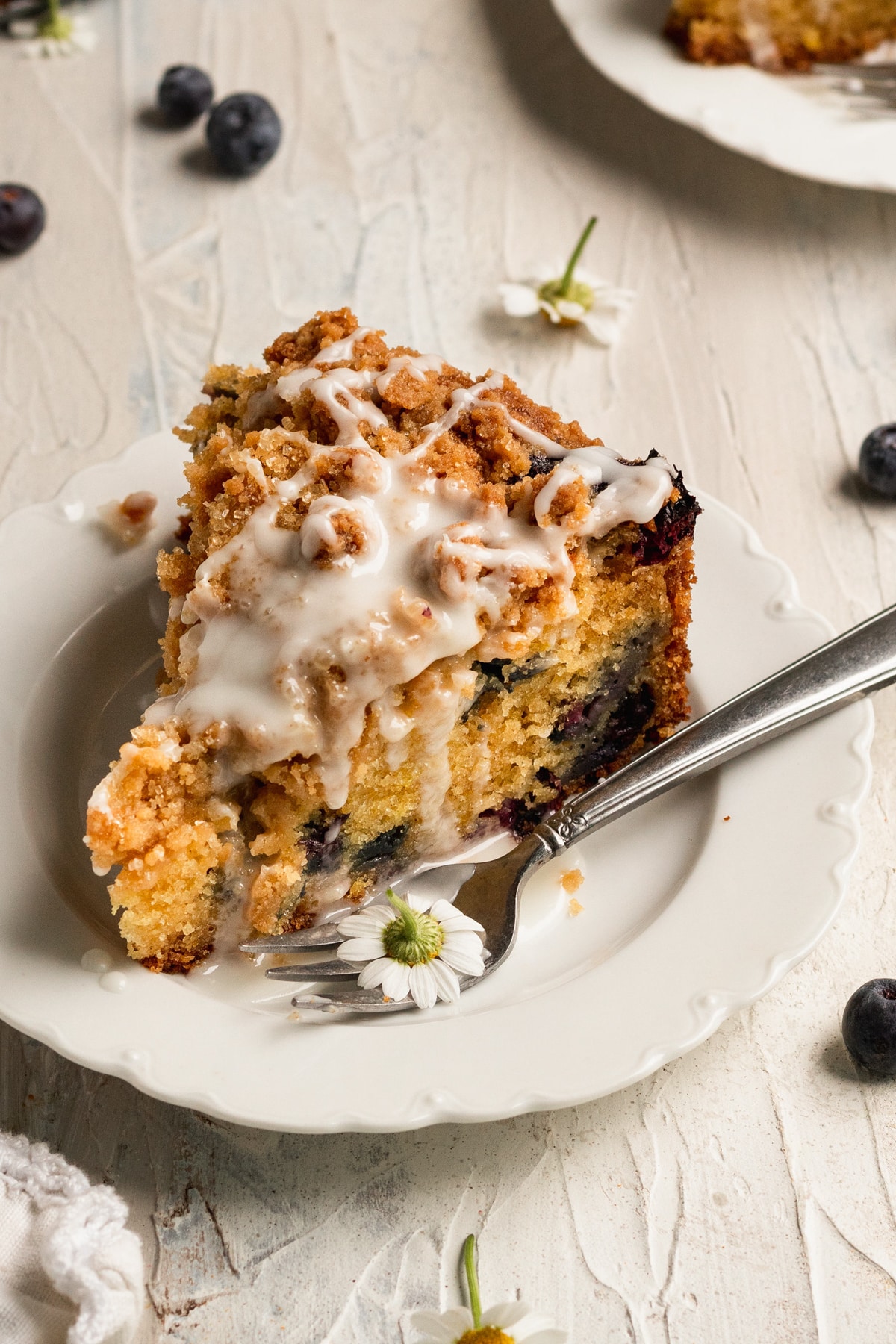 a slice of blueberry coffee cake on a white plate with a lemon glaze on top.