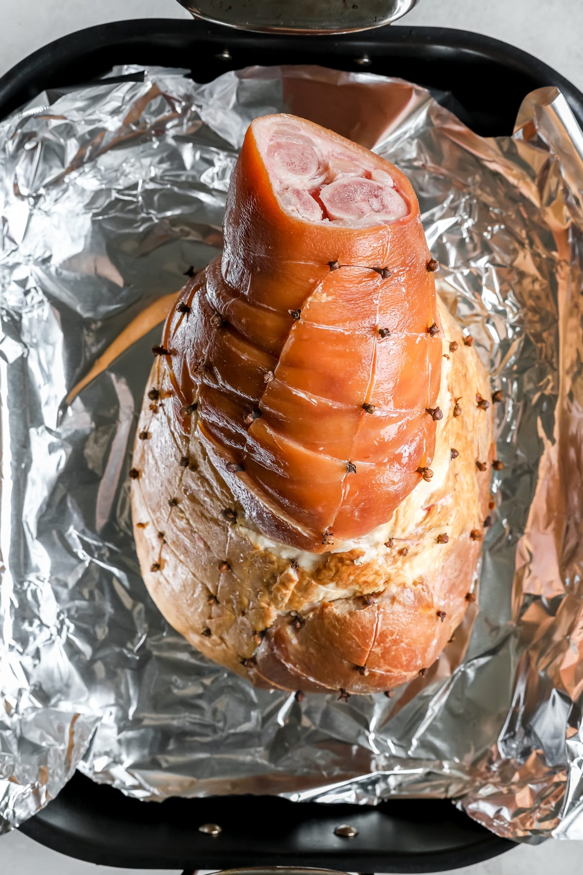 a fully-cooked bone-in ham in a roasting pan lined with foil that has been scored and with cloves in the crossing. 