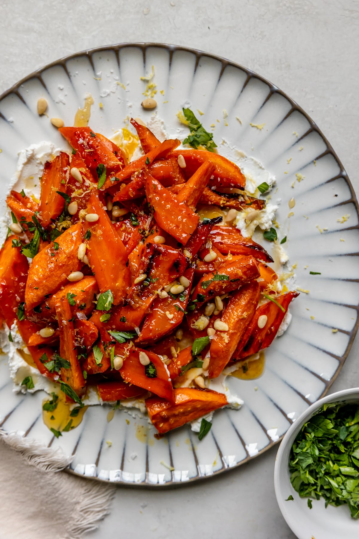 a plate smeared with goat cheese and topped with roasted carrots garnished with lemon zest, parsley, pine nuts and sea salt. 