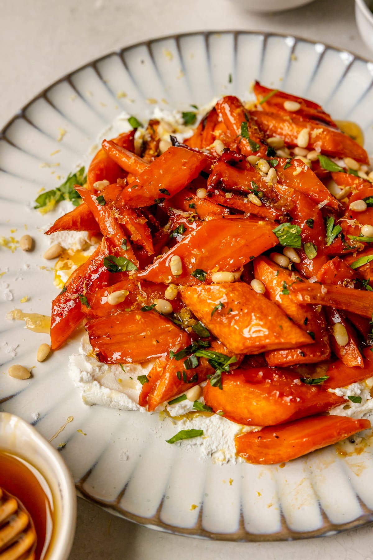 a plate smeared with goat cheese and topped with roasted carrots garnished with lemon zest, parsley, pine nuts and sea salt. 