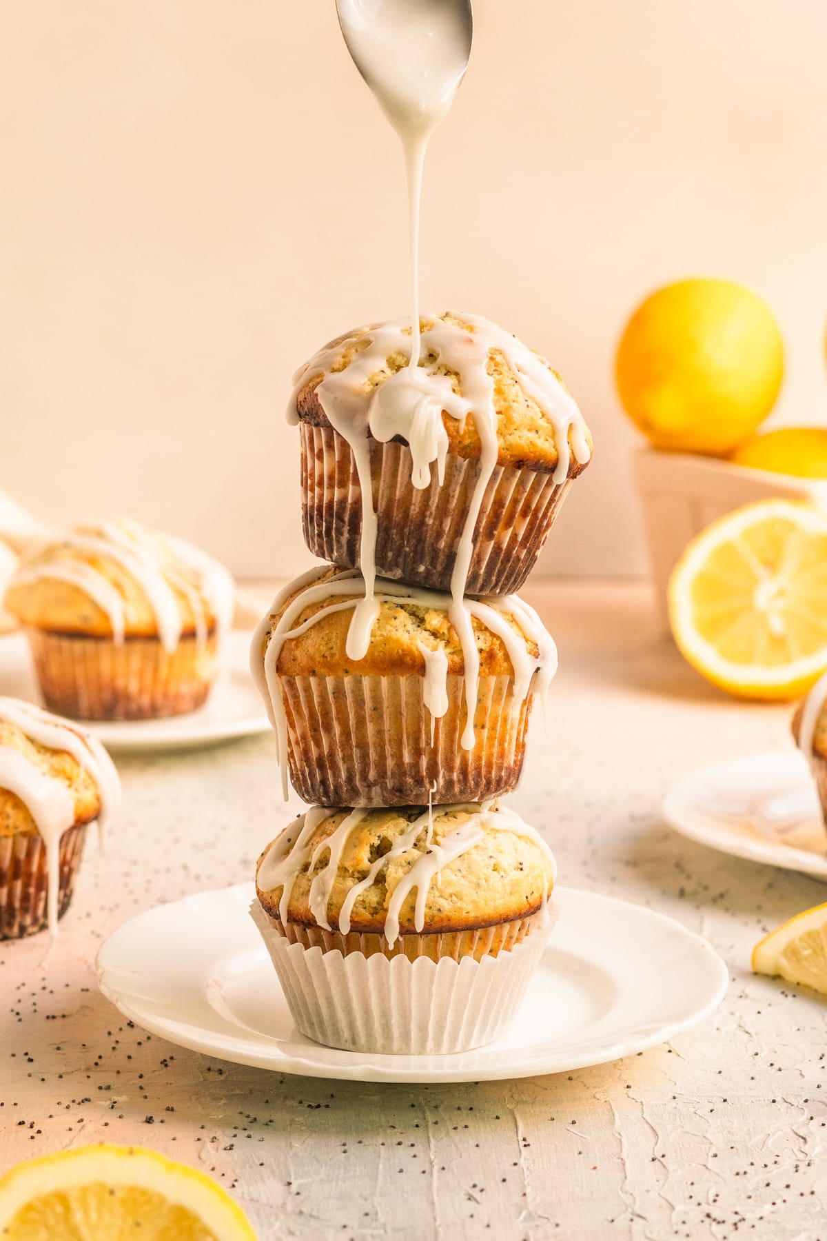 a stack of lemon poppyseed muffins on a white plate with glaze being drizzled on top. 