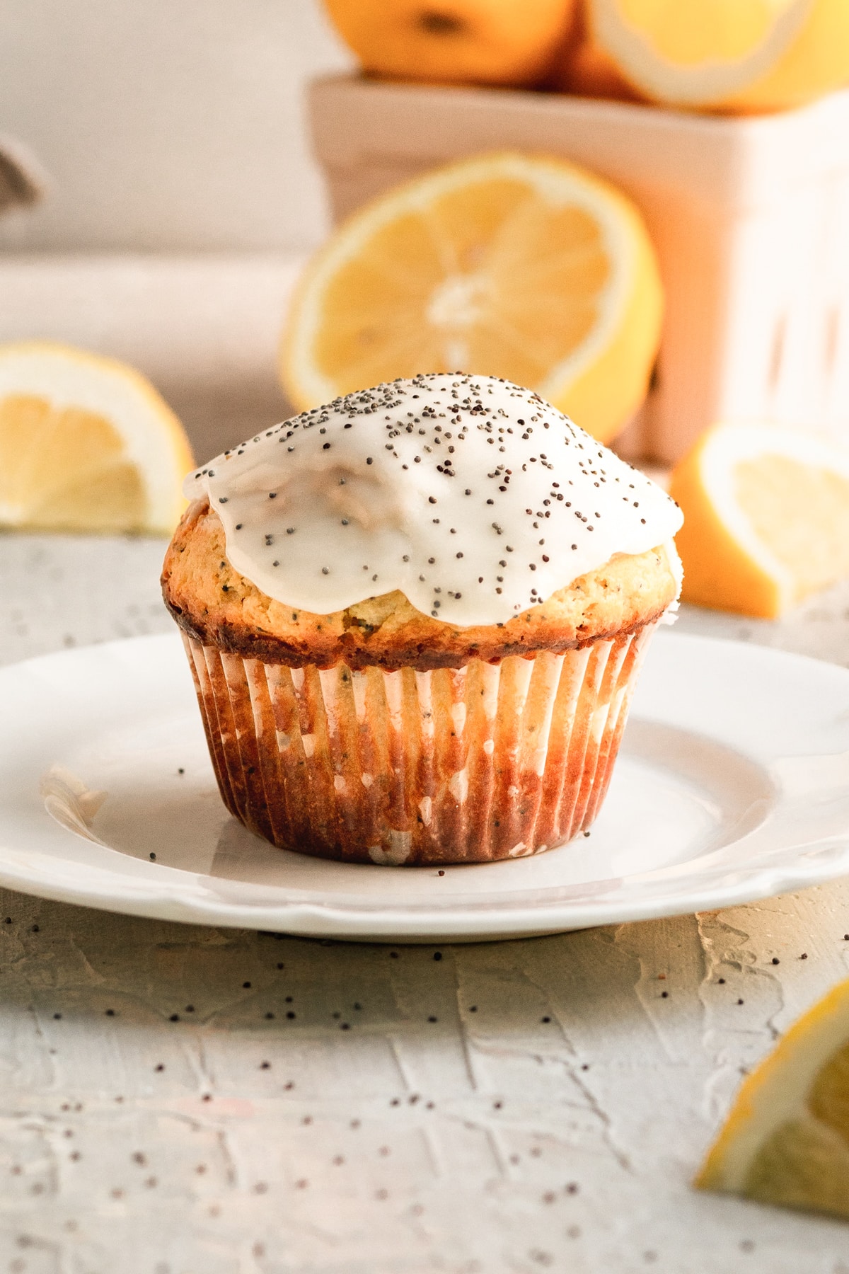 a muffin on a white plate with glaze and poppyseeds on top.