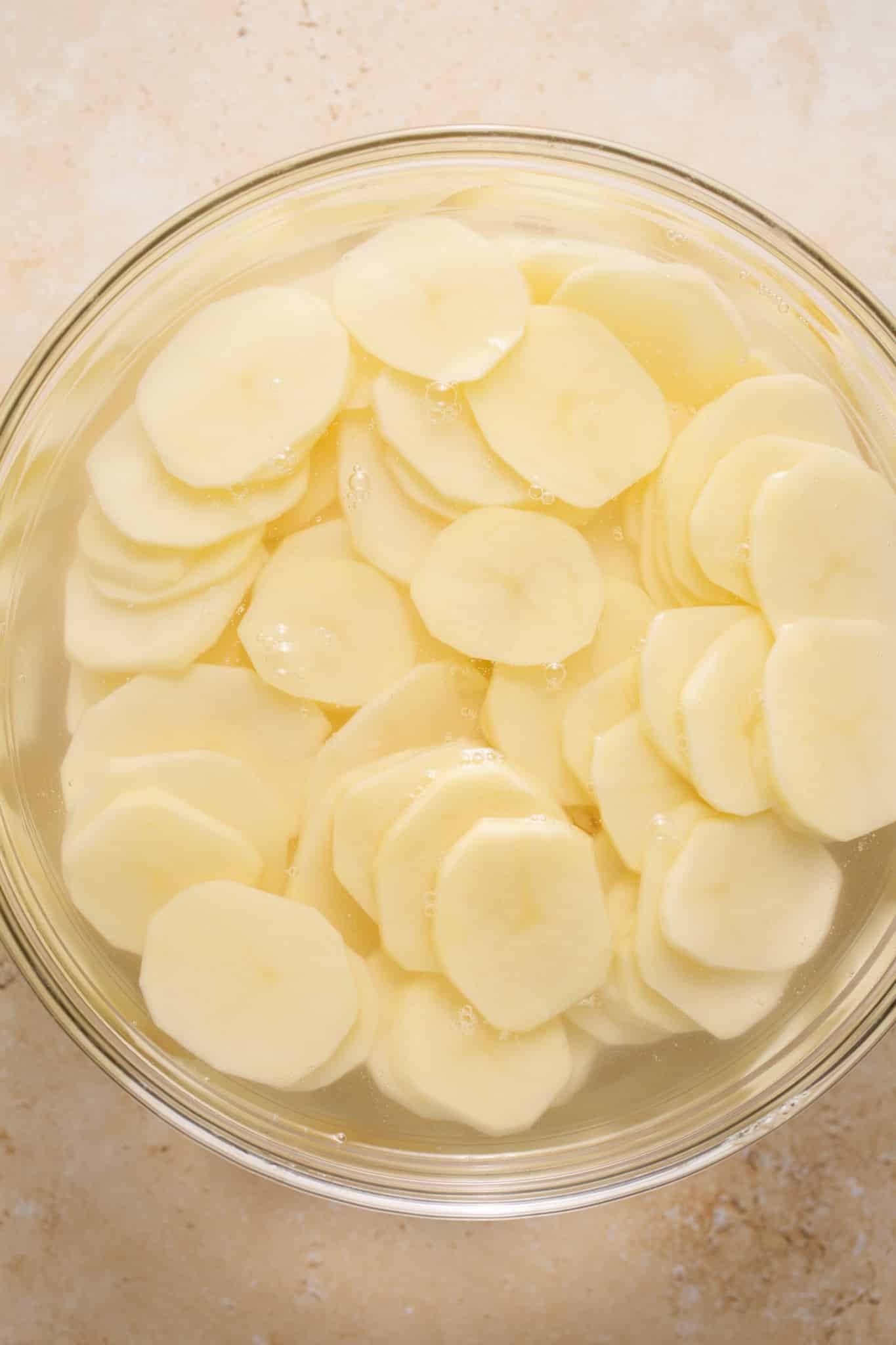 sliced potatoes in a large glass bowl with water. 