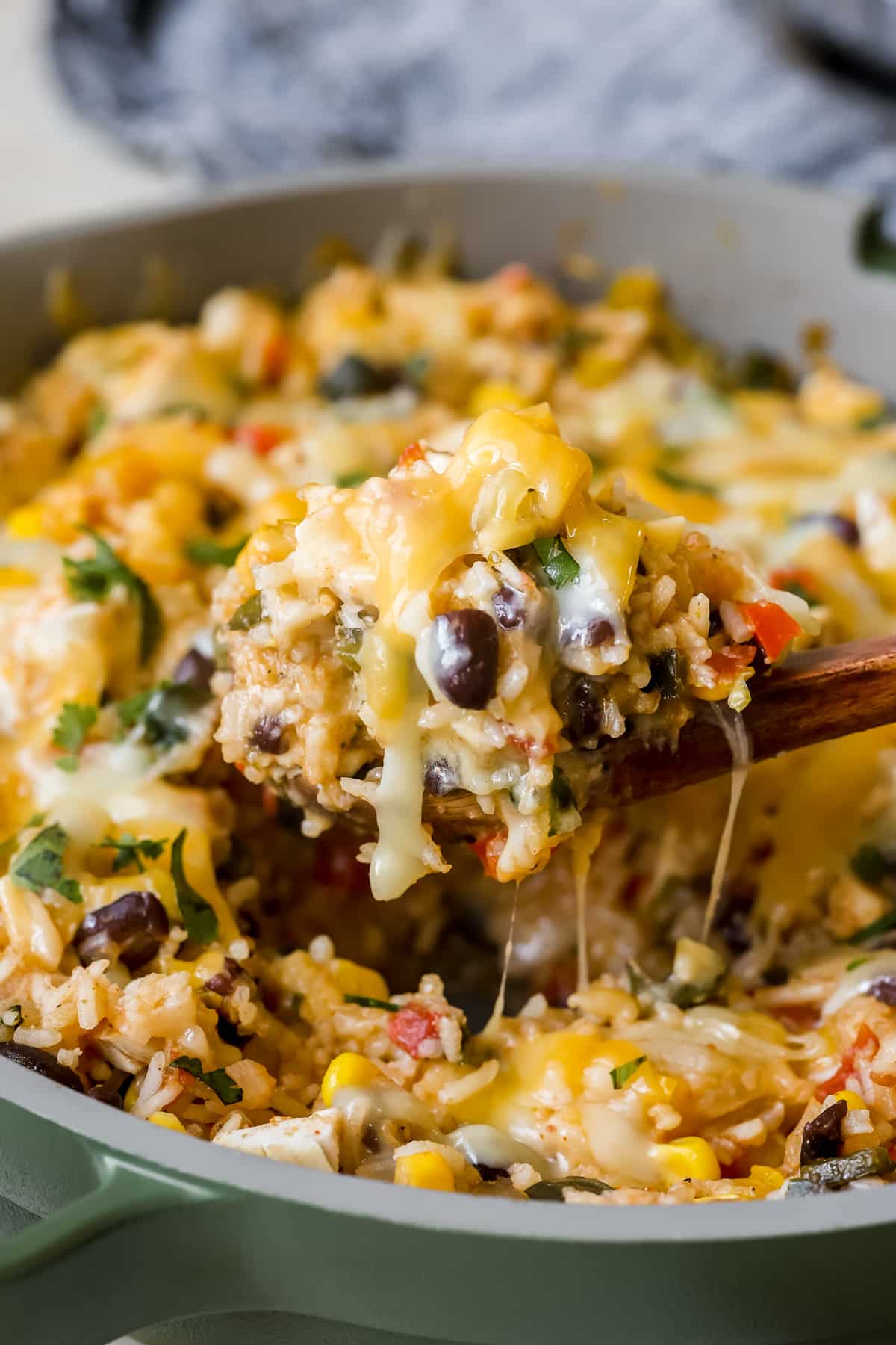 a wooden spoon scooping rice and beans out of a skillet with a cheesy pull.