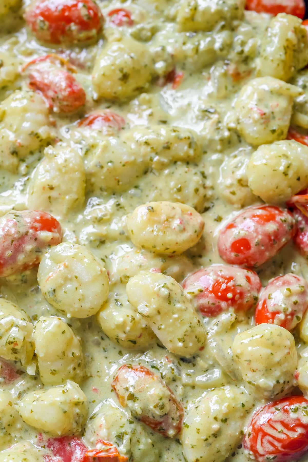an up close image of pesto, tomatoes and gnocchi. 
