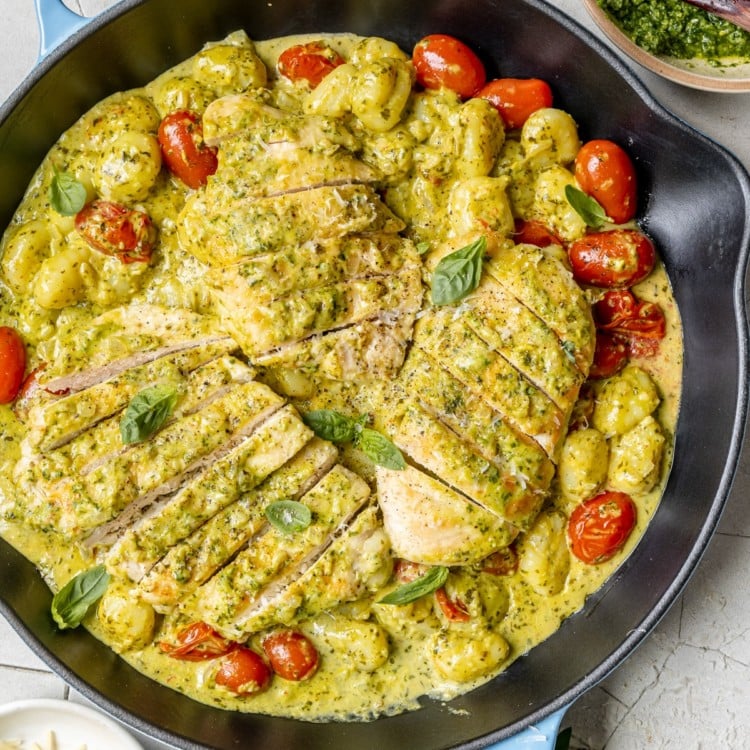 cast iron skillet with sliced chicken breast and cherry tomatoes covered in pesto sauce