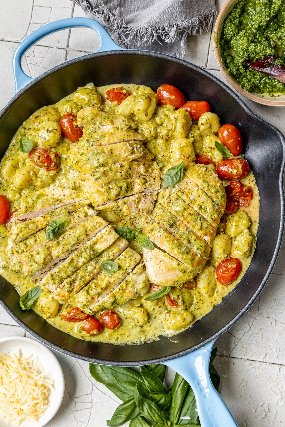 cast iron skillet with sliced chicken breast and cherry tomatoes covered in pesto sauce