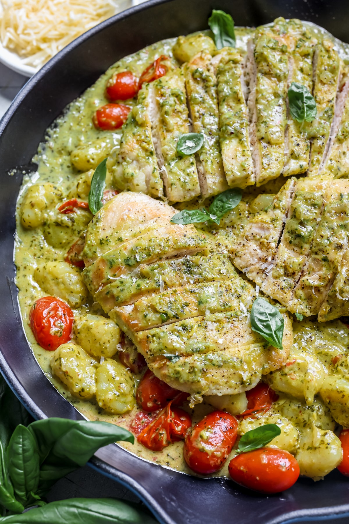 chicken, pesto and gnocchi in a skillet garnished with basil and black pepper. 