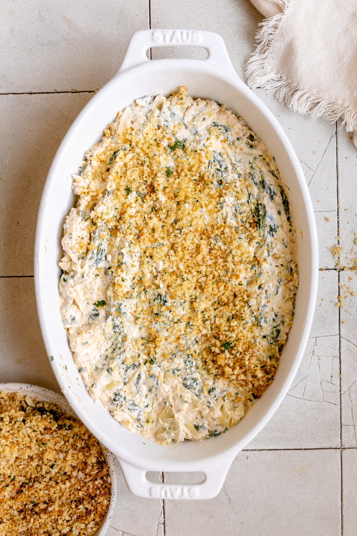 spinach dip in a white casserole dish topped with Panko breadcrumbs. 
