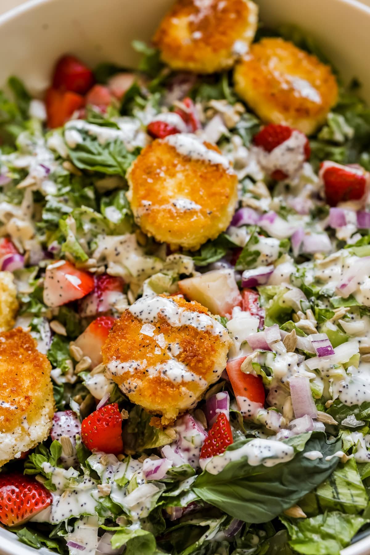 salad in a large white bowl with fried goat cheese, poppyseed dressing, and strawberries. 