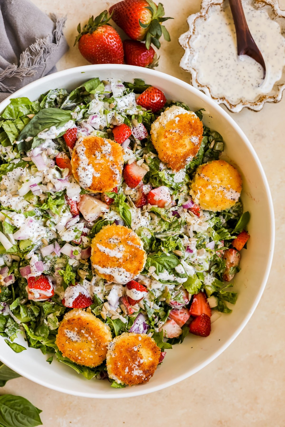 salad in a large white bowl with fried goat cheese, poppyseed dressing, and strawberries. 