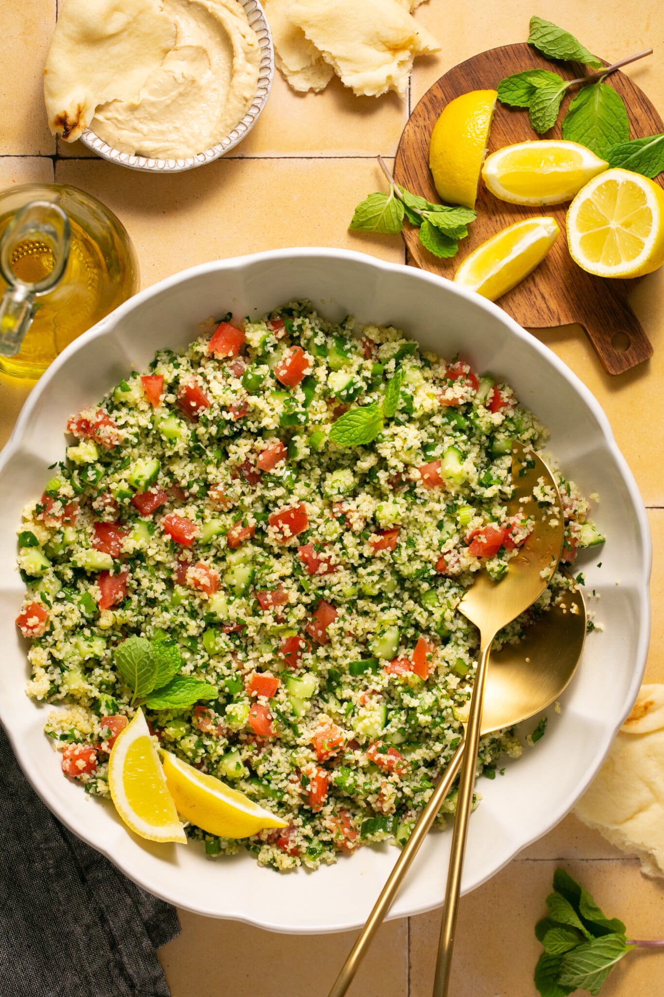 a bowl filled with fresh ingredients for salad with gold serving spoons. 