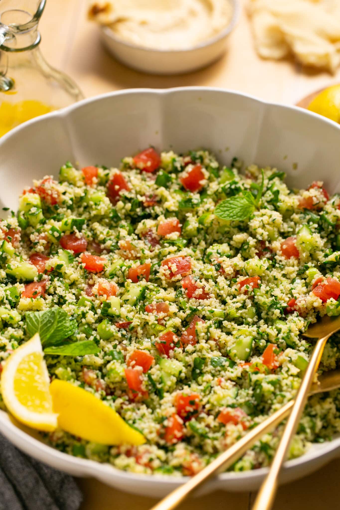 a bowl filled with fresh ingredients for salad with gold serving spoons. 