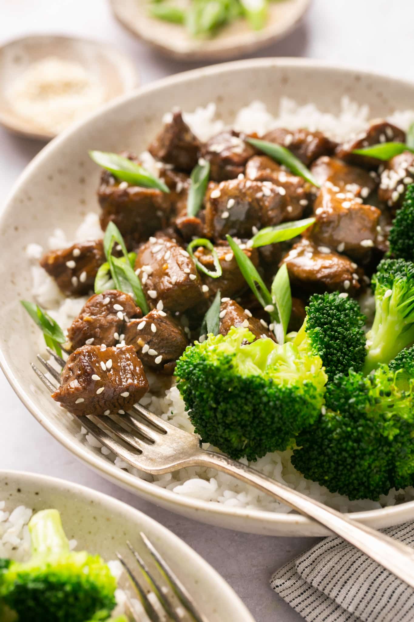 steak bites in a bowl over with with broccoli and garnished with green onions and sesame seeds. 