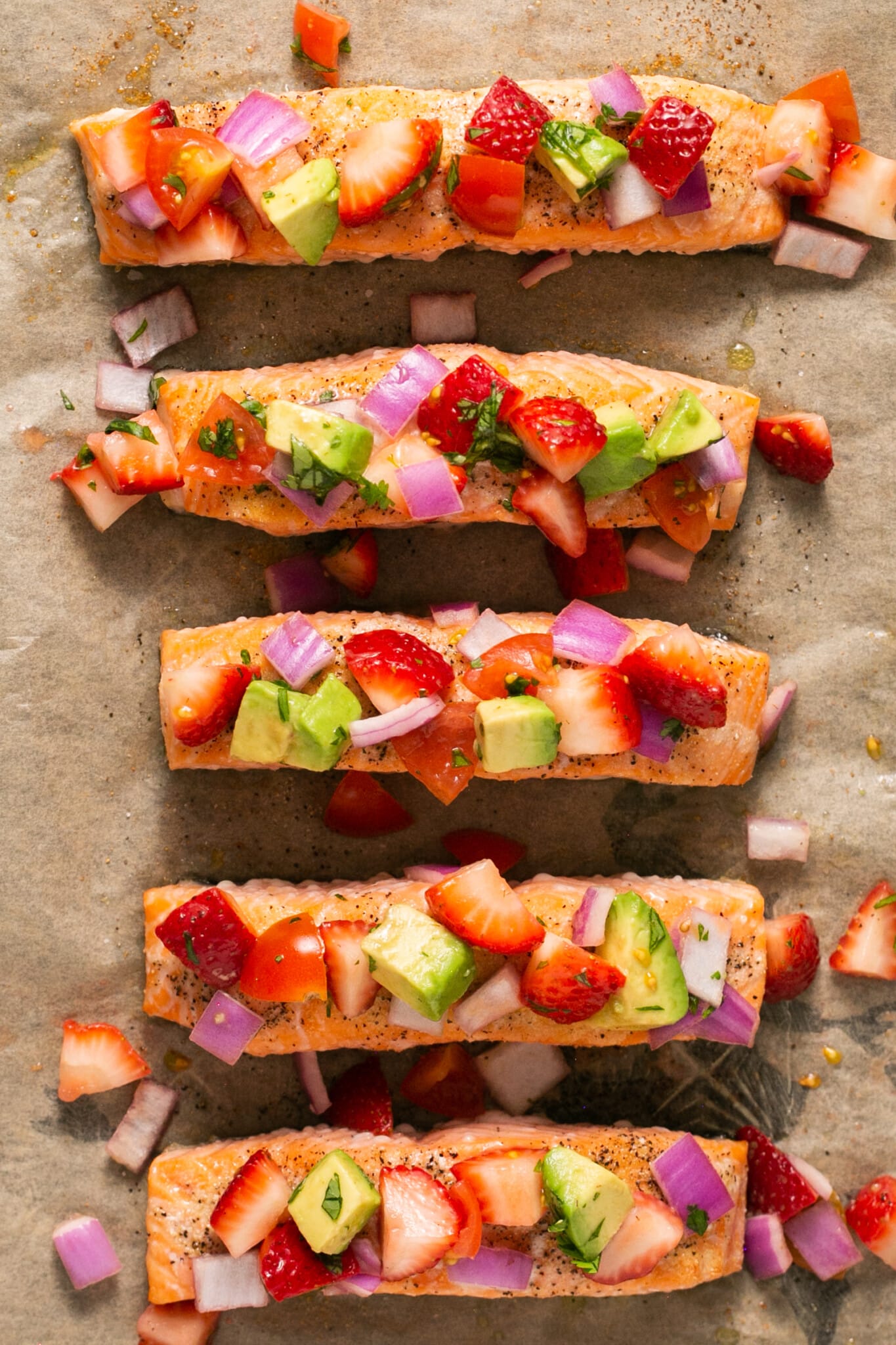 strawberry salsa on top of salmon fillets on a sheet pan lined with parchment paper. 