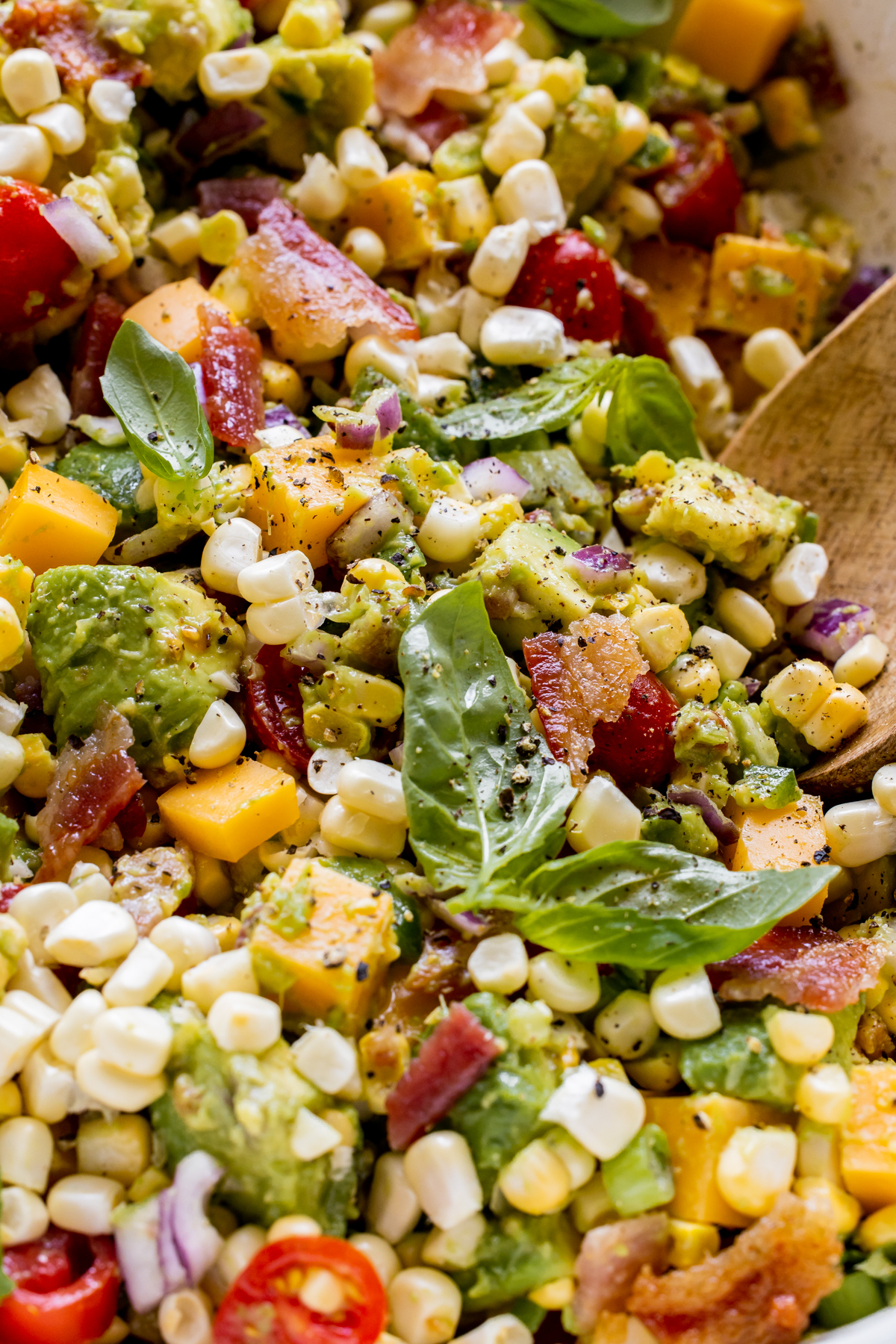 a close up image of avocado corn salad garnished with basil and black pepper. 