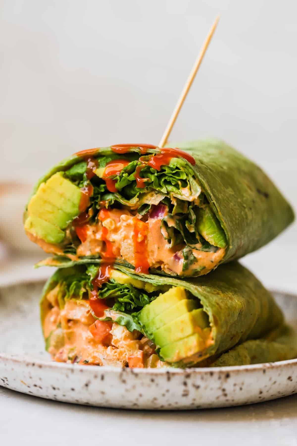 buffalo chicken in a spinach wrap with avocado and lettuce and buffalo sauce dripping down. 
