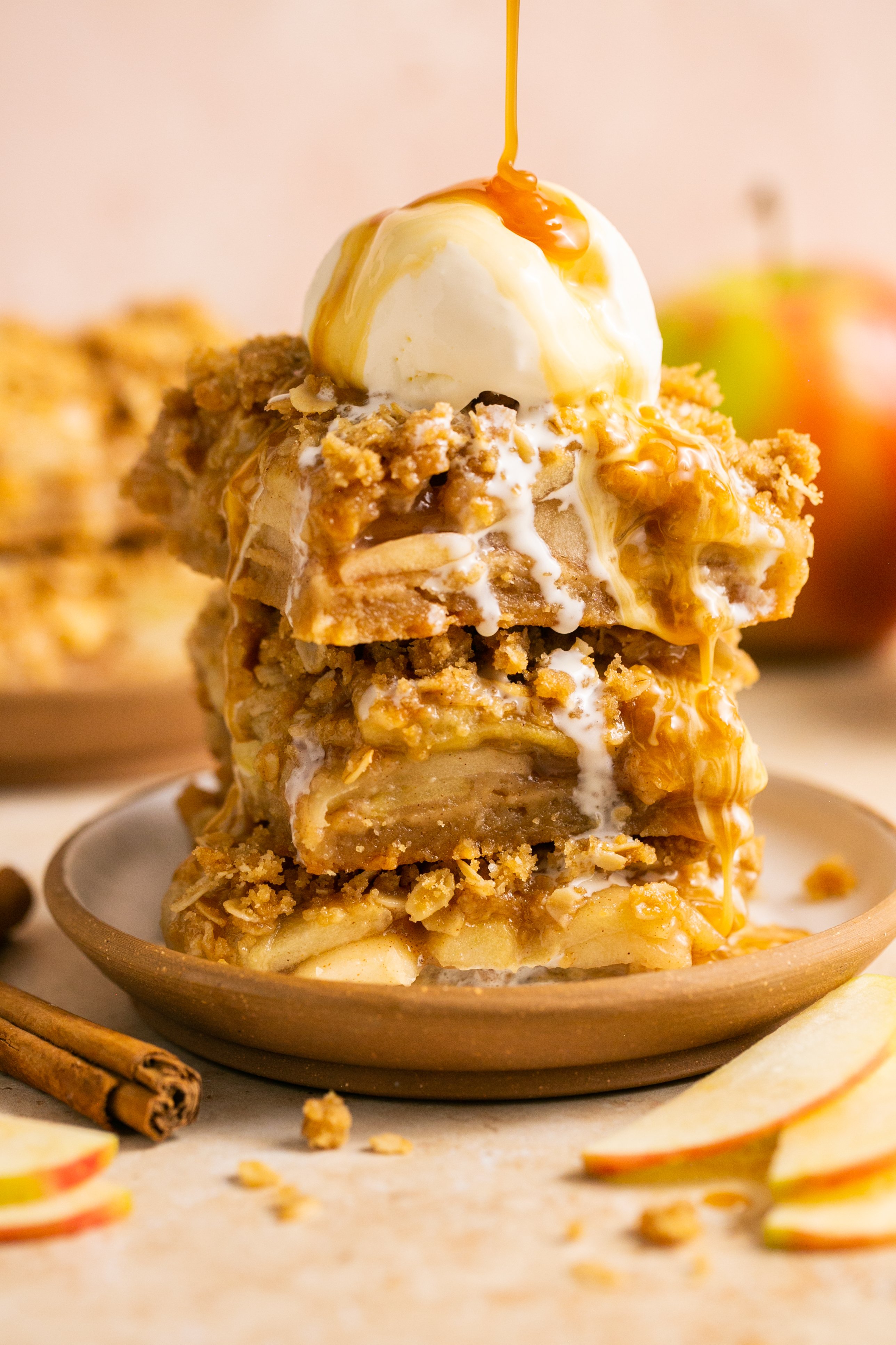 A stack of apple pie bars with ice cream and caramel on top. 