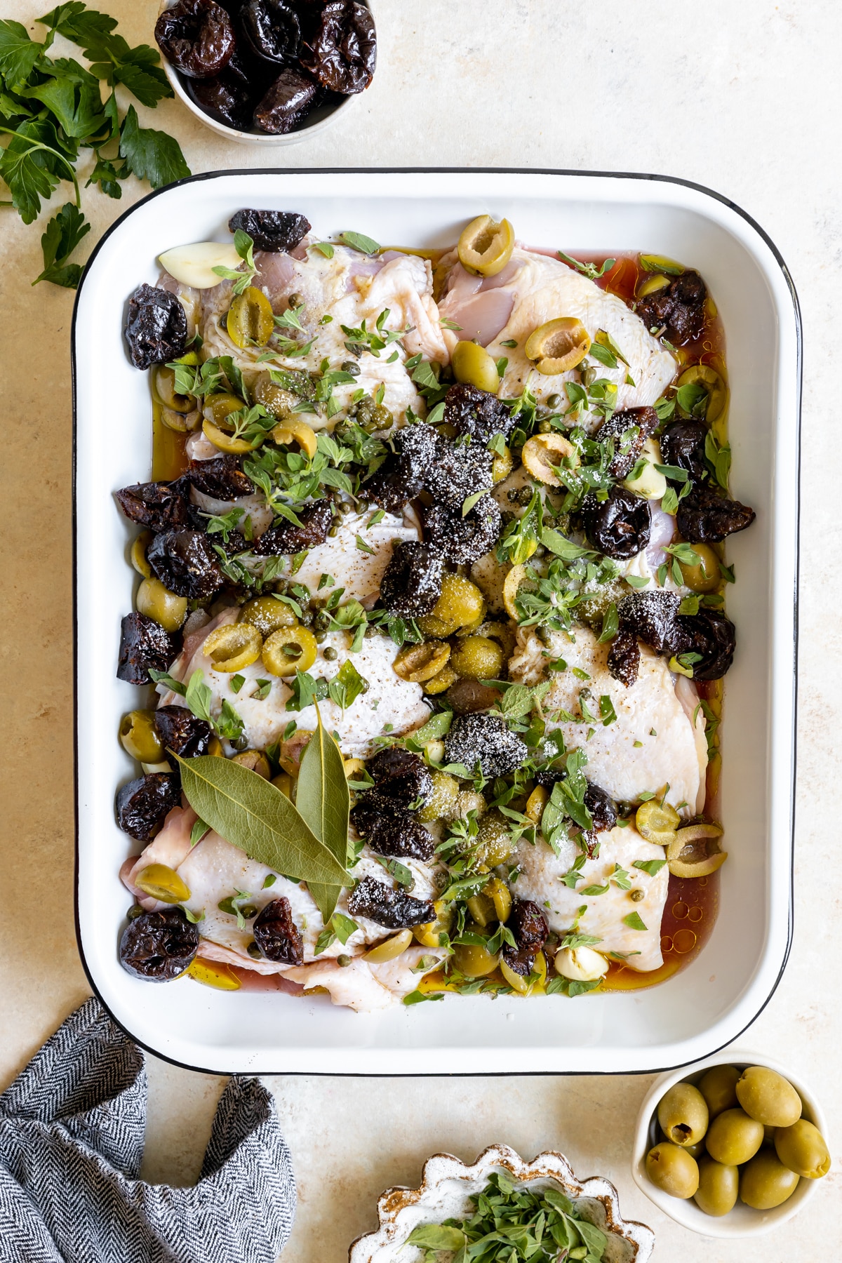 chicken thighs in a roasting pan with olives, prunes, fresh herbs, olive oil and red wine vinegar. 