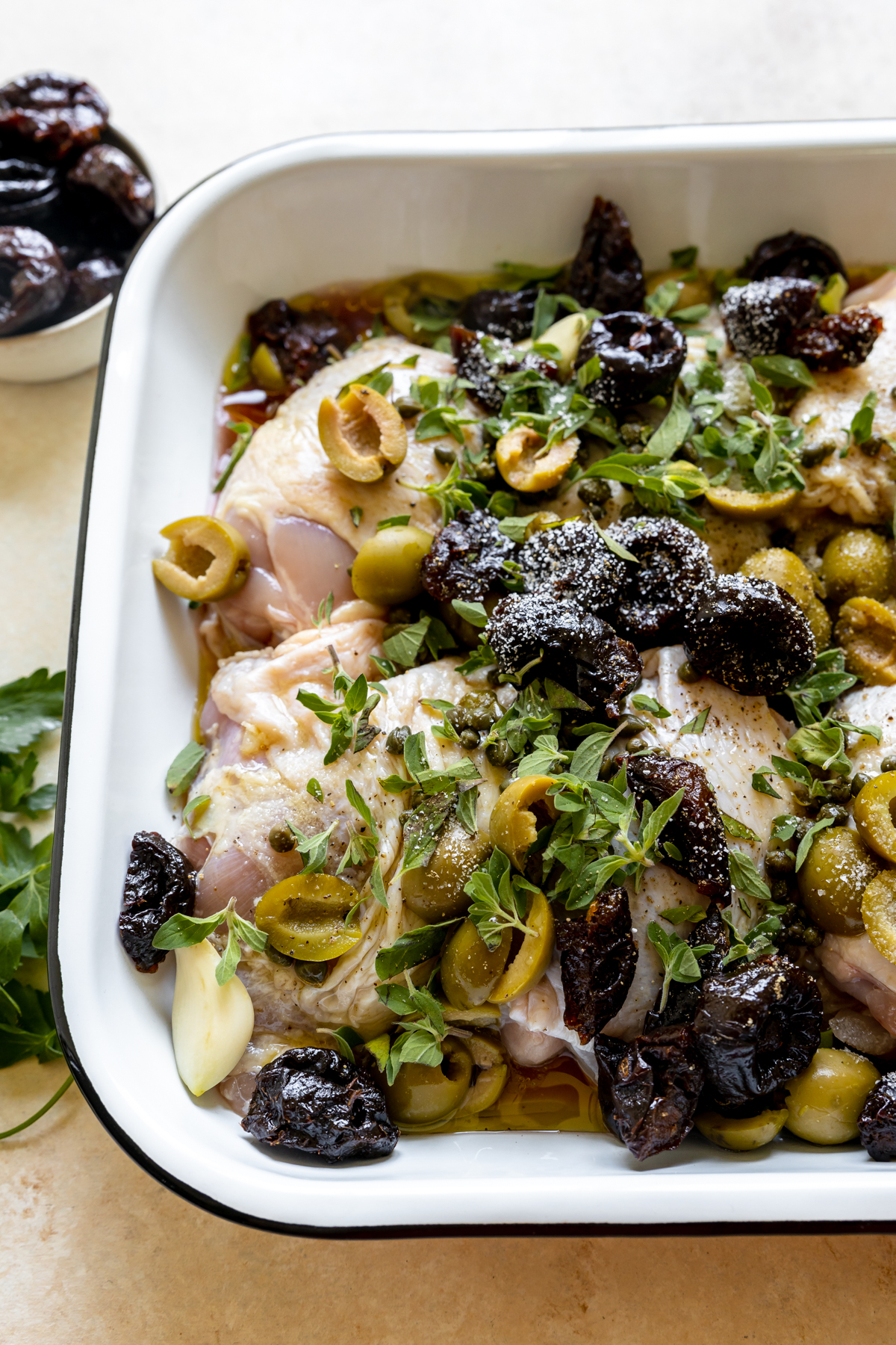 chicken thighs in a roasting pan with olives, prunes, fresh herbs, olive oil and red wine vinegar. 