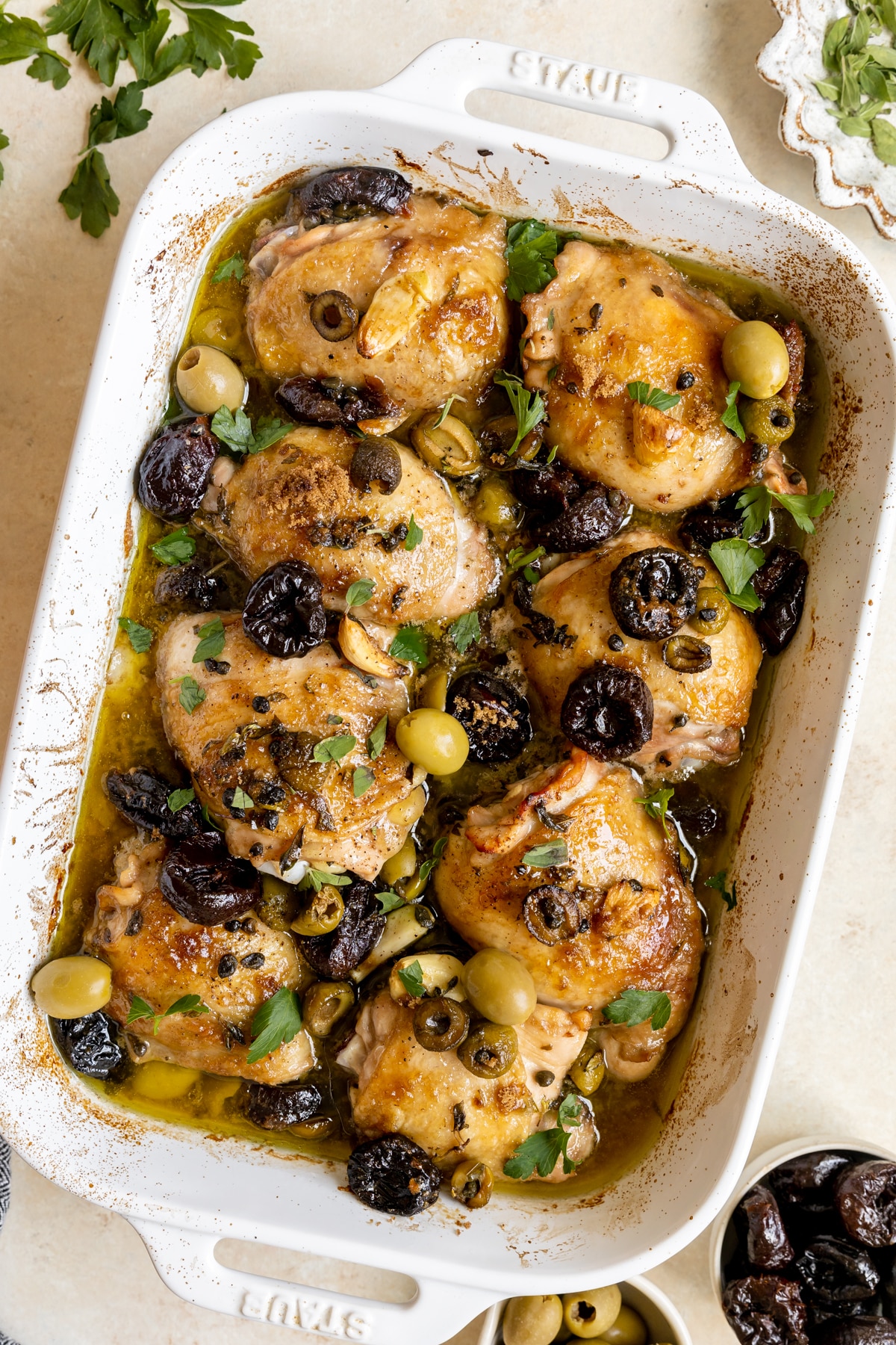 chicken in a 9x13 inch white glass baking dish topped with prunes and olives. 