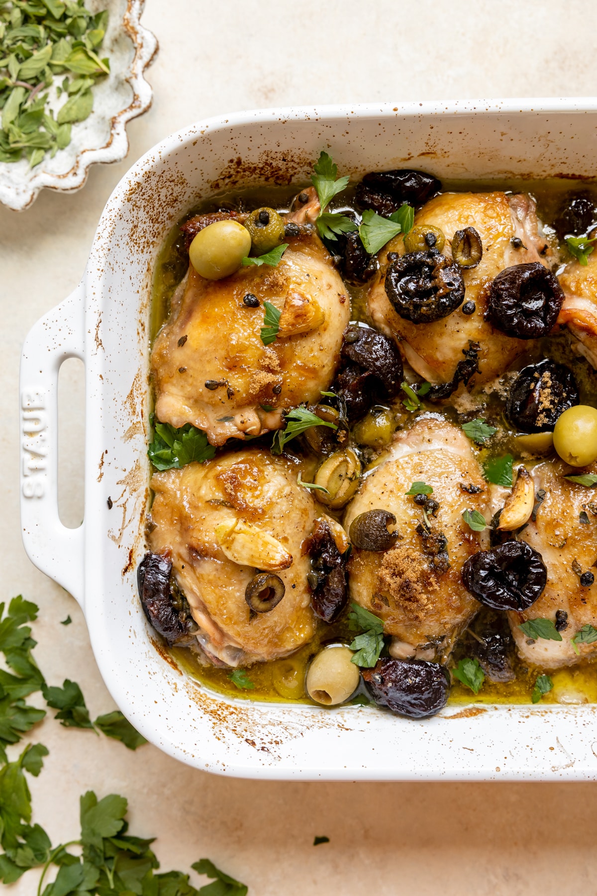 chicken thighs in a roasting pan with olives, prunes, fresh herbs, olive oil and red wine vinegar. 