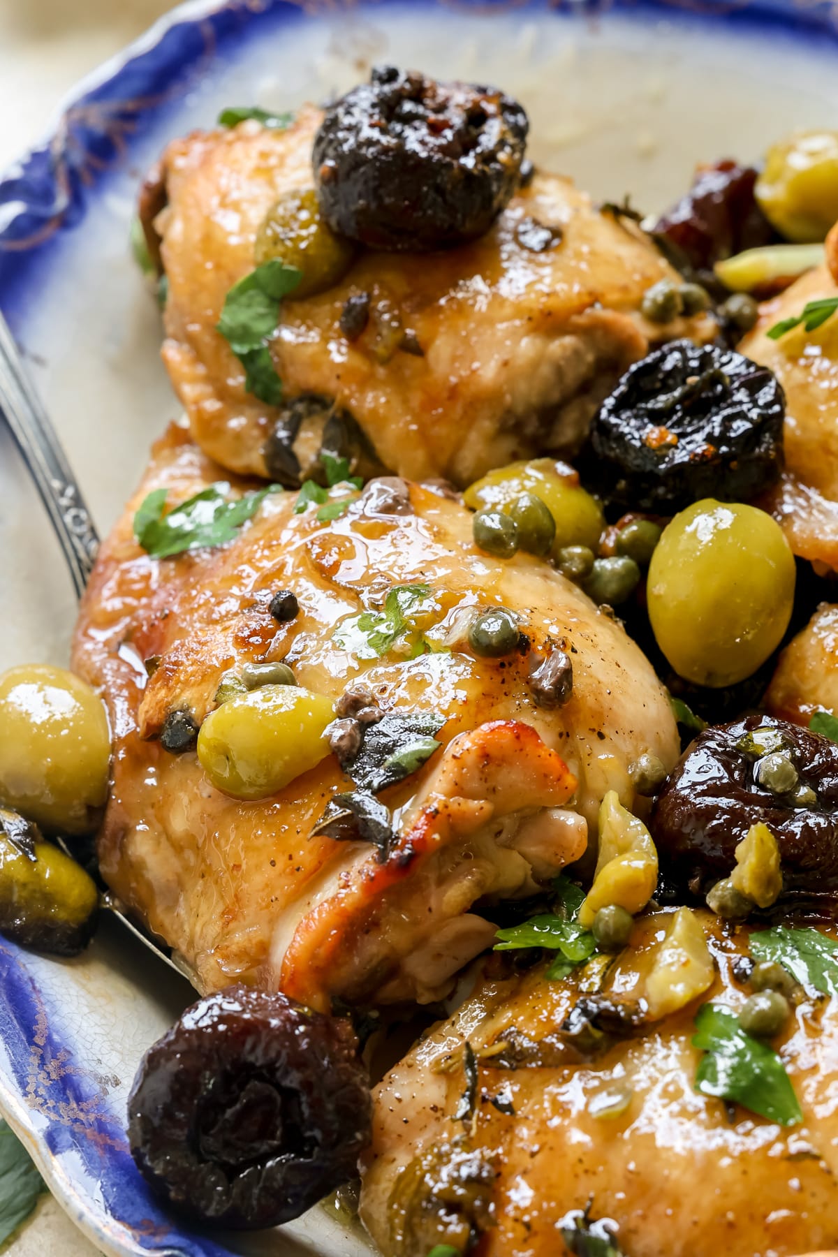 an up close image on a chicken thigh with capers, prunes, olives and parsley garnished on top. 
