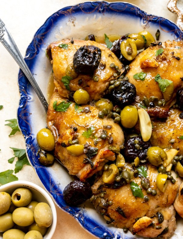 chicken thighs with green and black olives and spices on a blue plate
