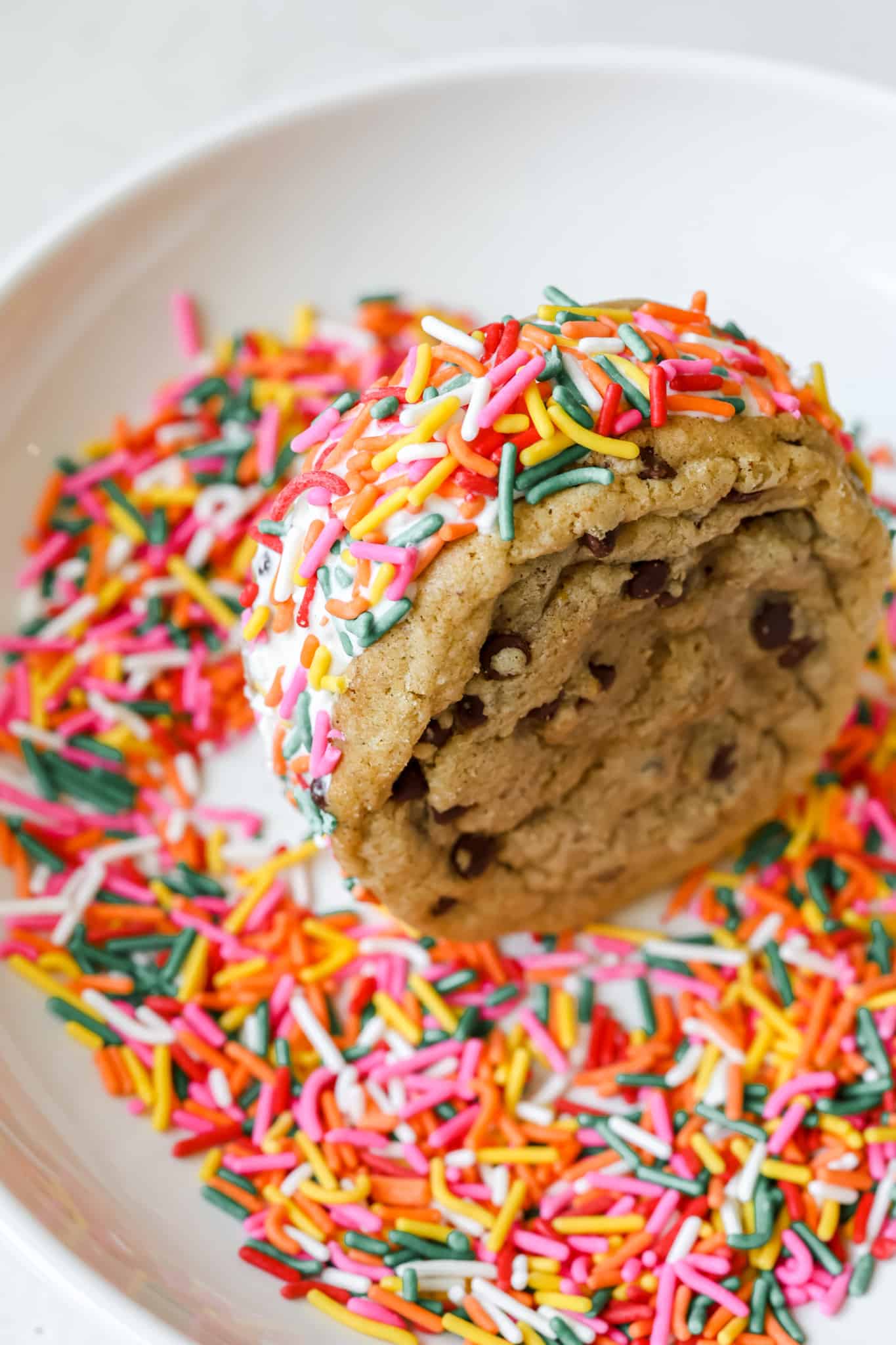 cookie sandwich being rolled in colorful sprinkles.