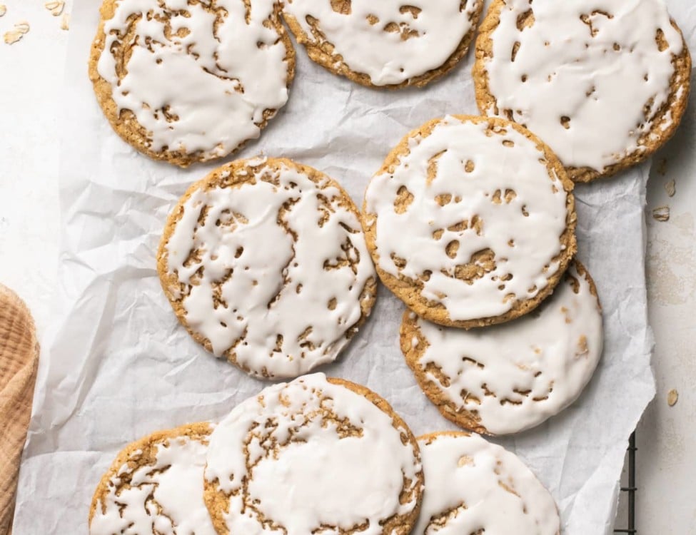 cooling rack topped with parchment paper with large, thin oatmeal cookies with white icing
