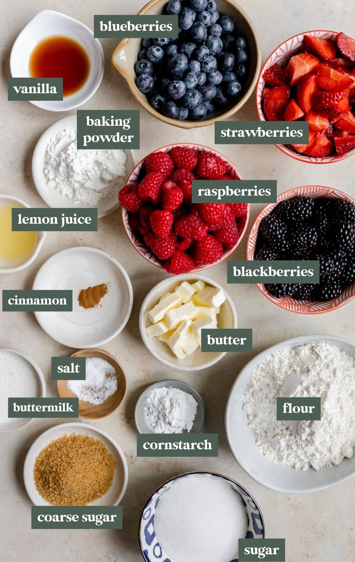 Bowls containing vanilla, berries, baking powder, lemon juice, cornstarch, salt, sugar, flour, and course flour to make mixed berry cobbler.