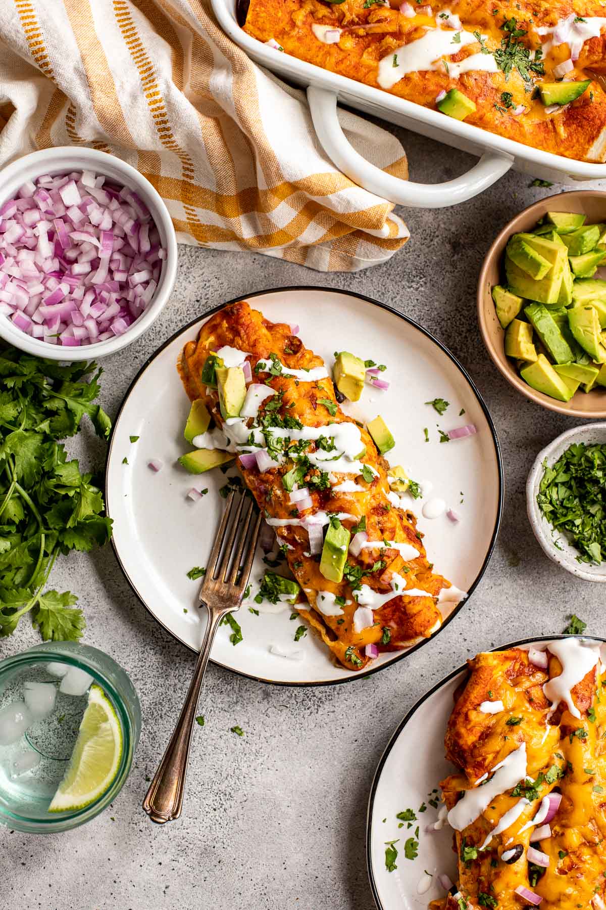 enchiladas on a white plate garnished with sour cream, avocado, cilantro and red onions. 