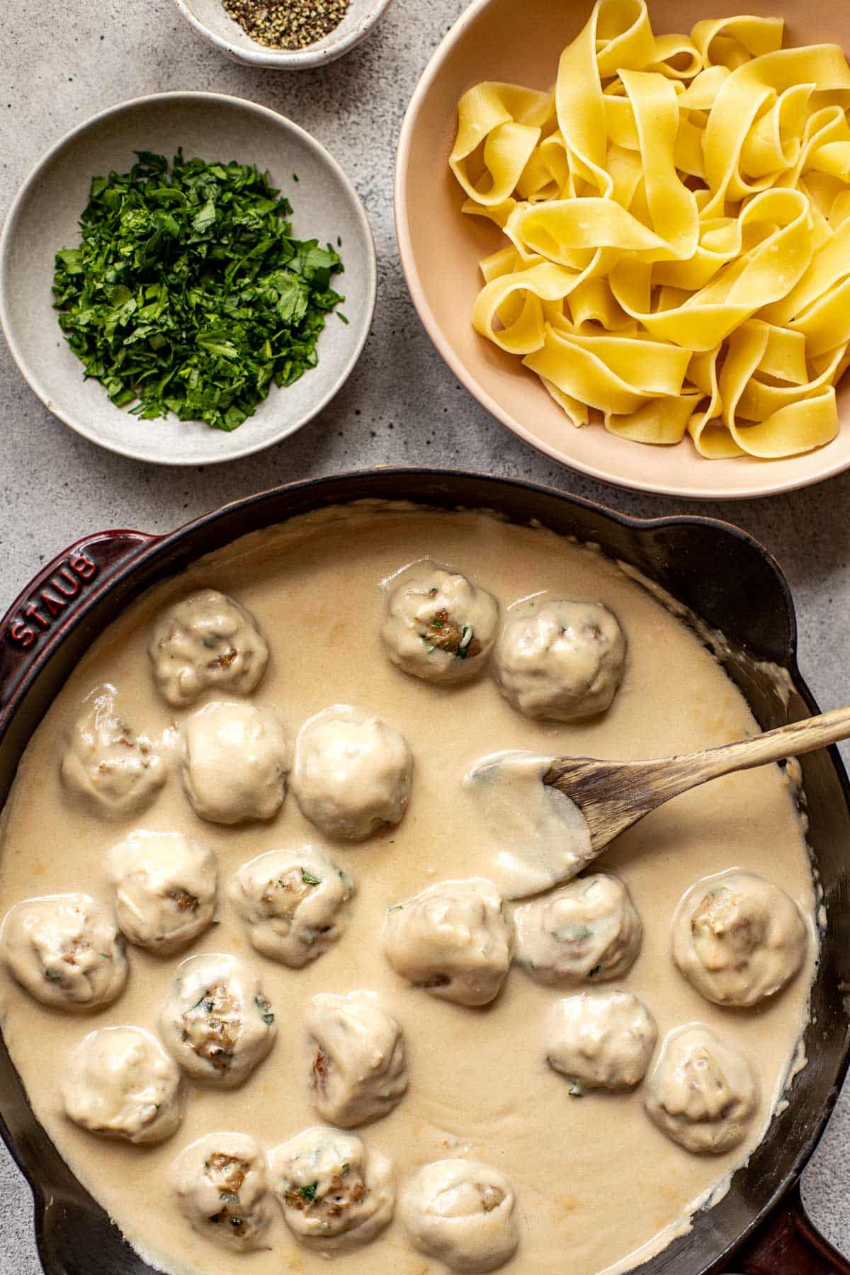 swedish meatballs in a skillet with parsley and pasta on the side. 