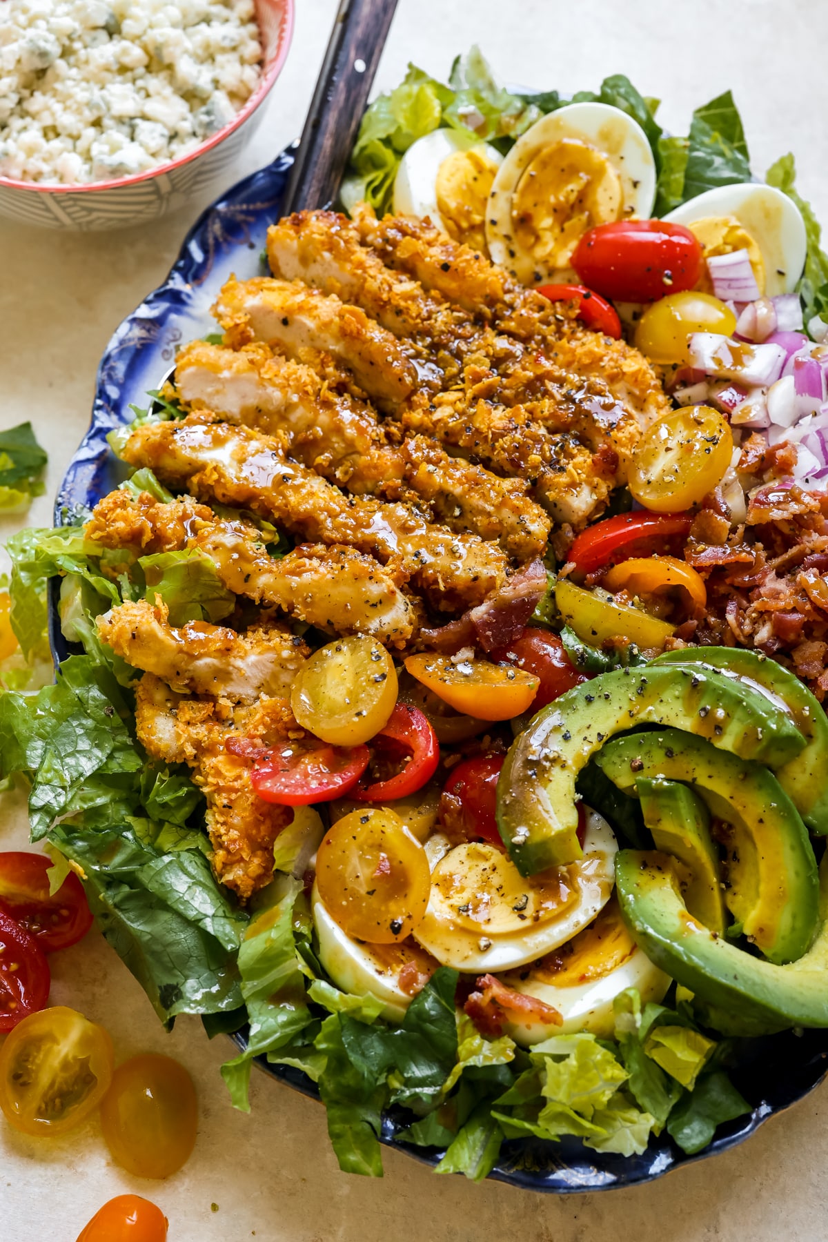 a cobb salad on a blue platter with dressing on top and crispy chicken. 