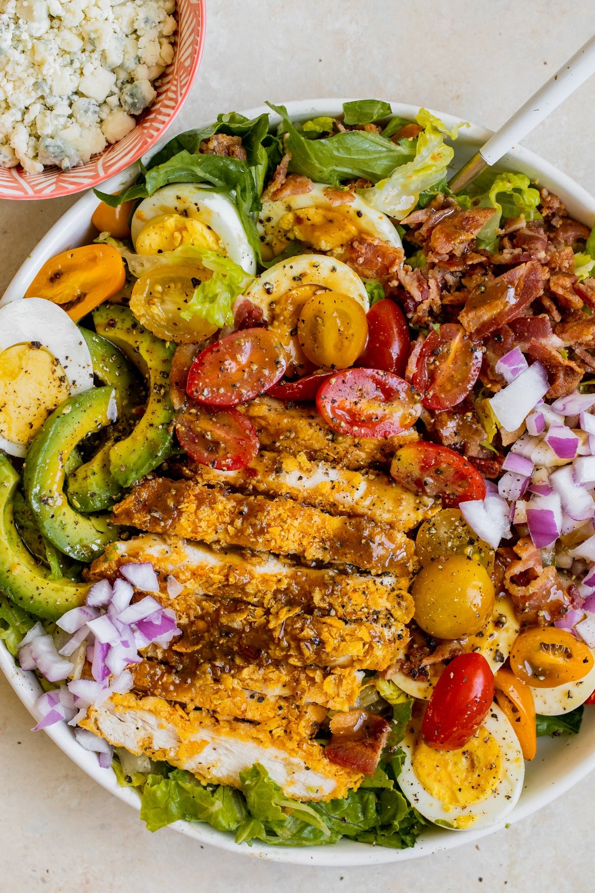 a cobb salad in a white bowl with dressing on top and crispy chicken. 
