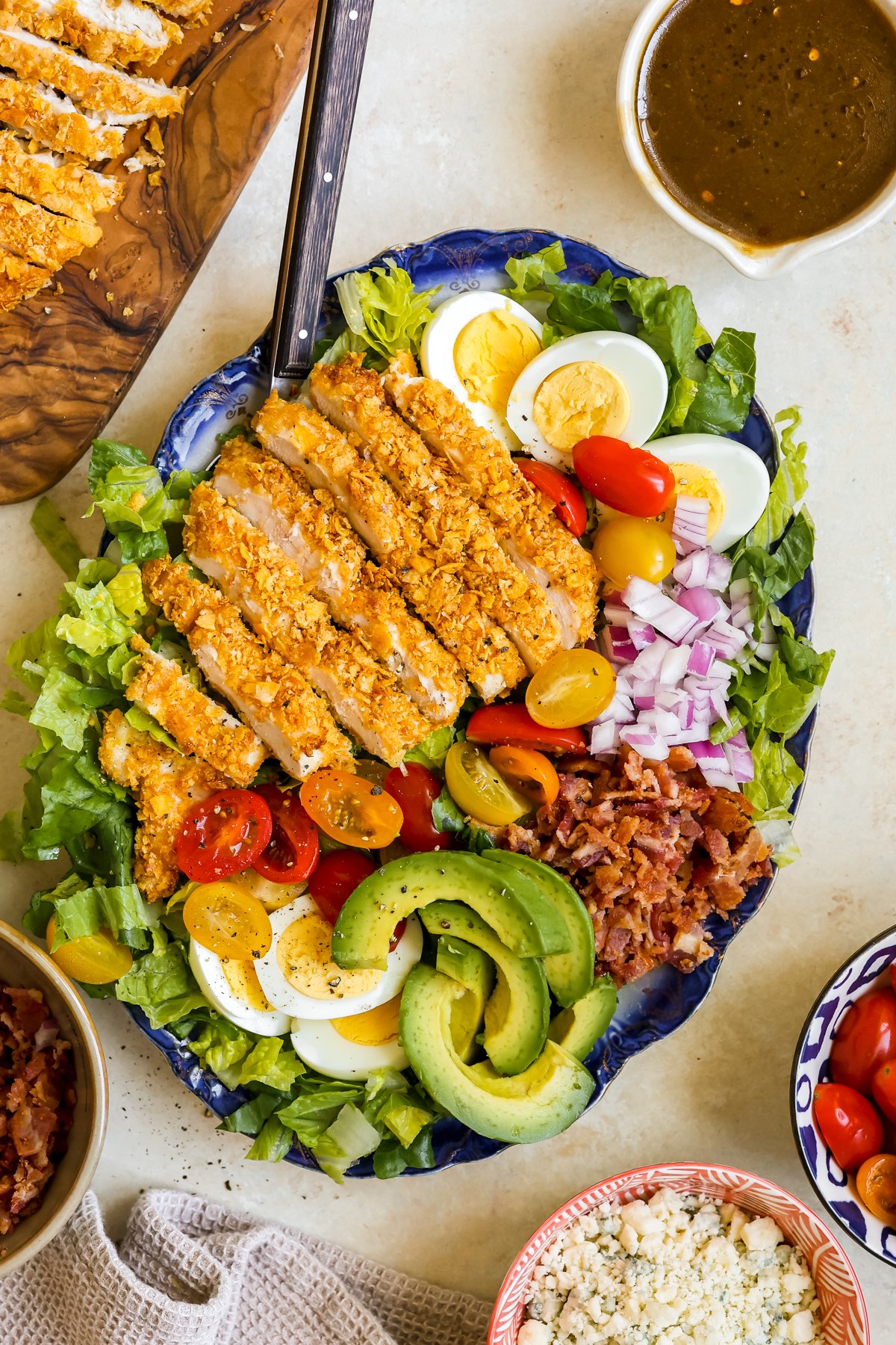 a cobb salad on a blue platter with crispy chicken and dressing on the side. 