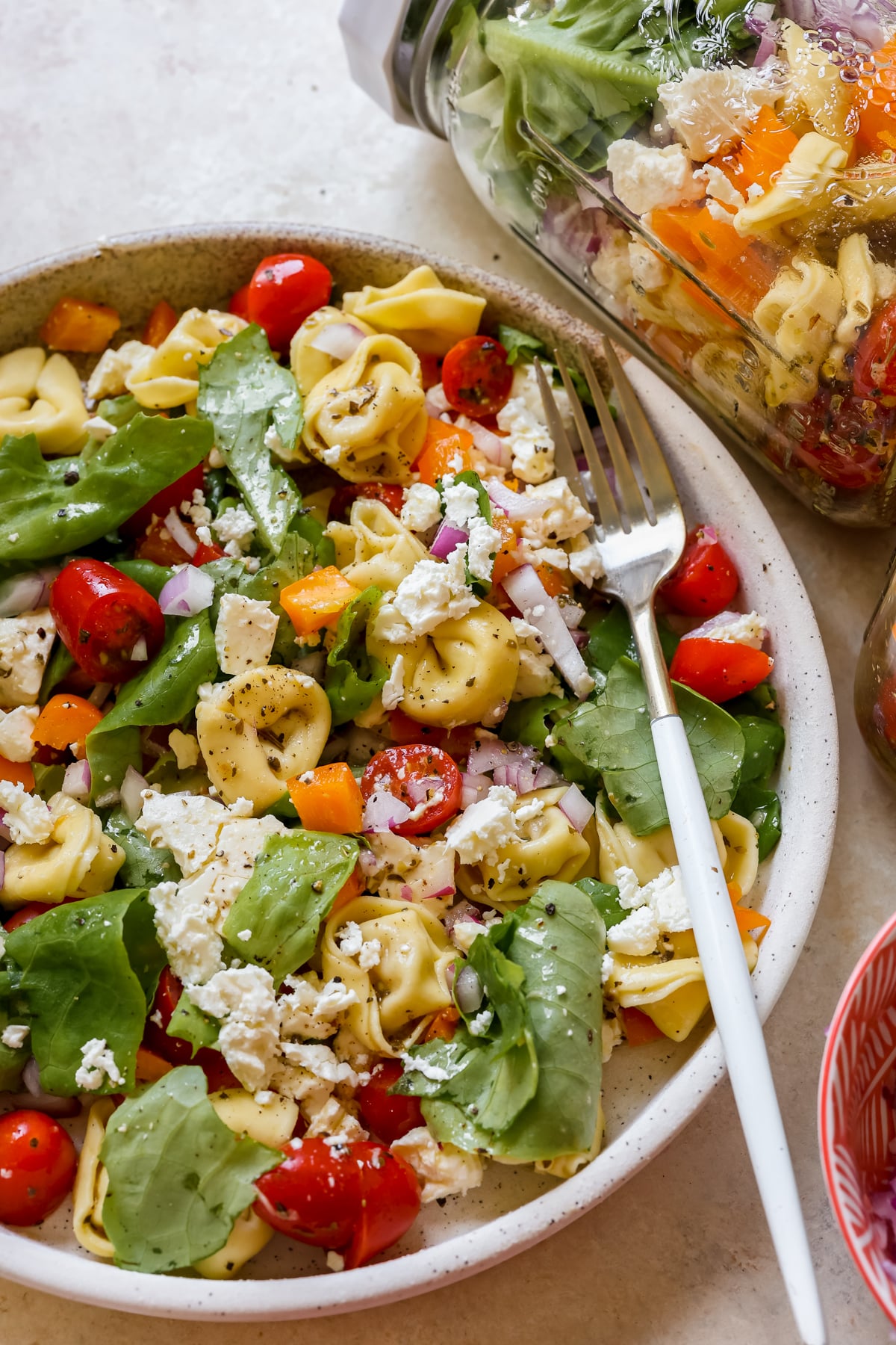 a tortellini salad on a white speckled plate. 