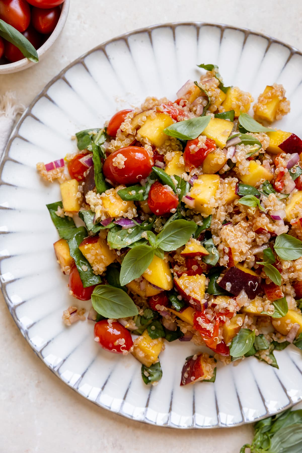 salad on a white plate with fresh basil, quinoa, cherry tomatoes, peaches and red onion. 