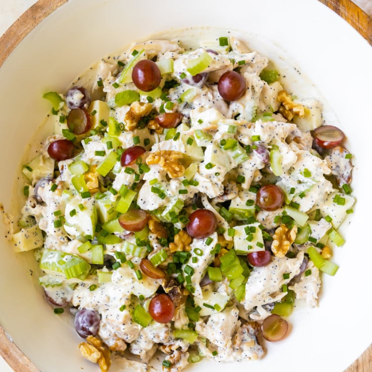 white bowl filled with chopped chicken, grapes, walnuts, apples, celery and a poppyseed dressing